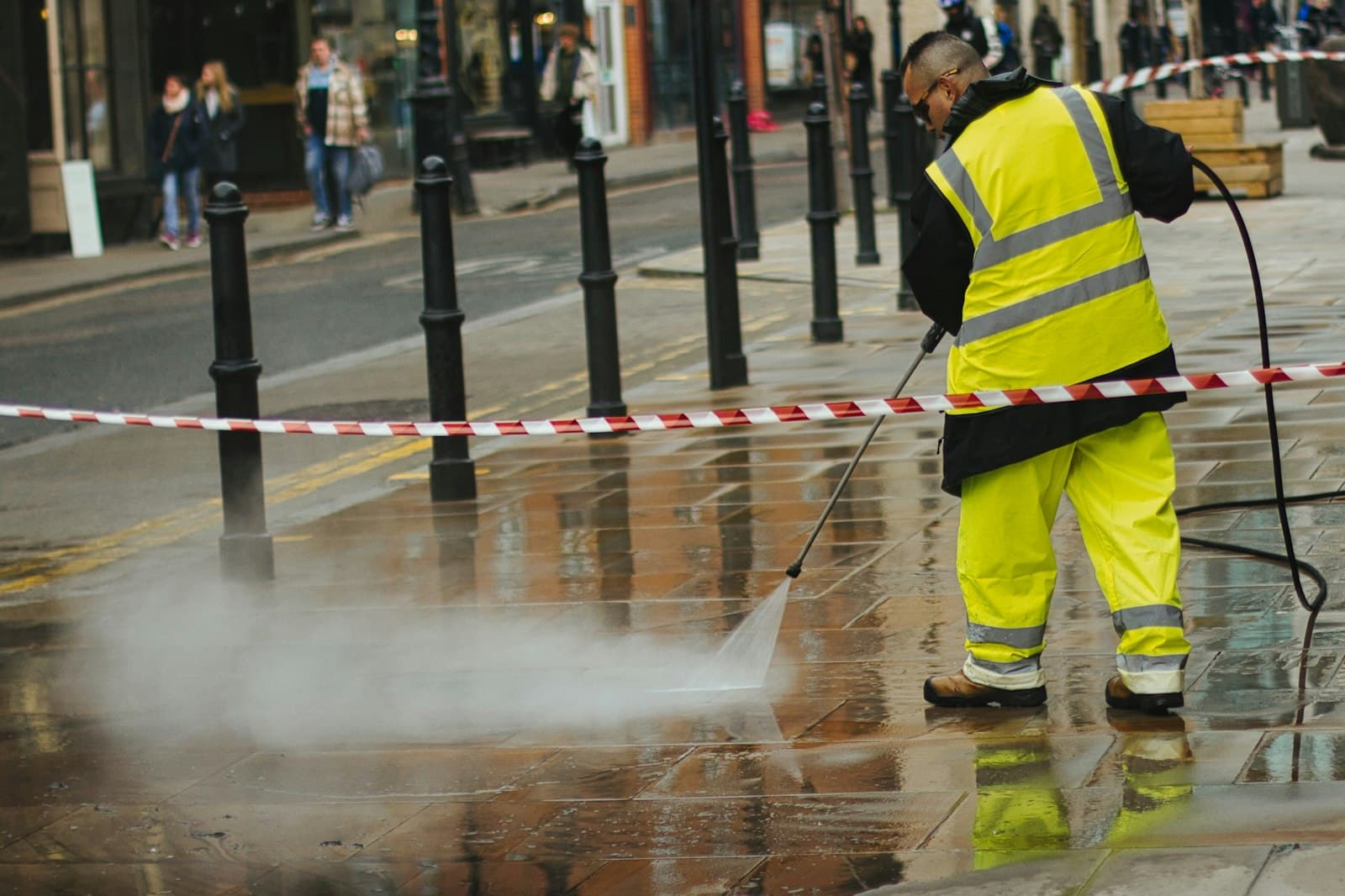 Worker in hi-vis pressure washing paving